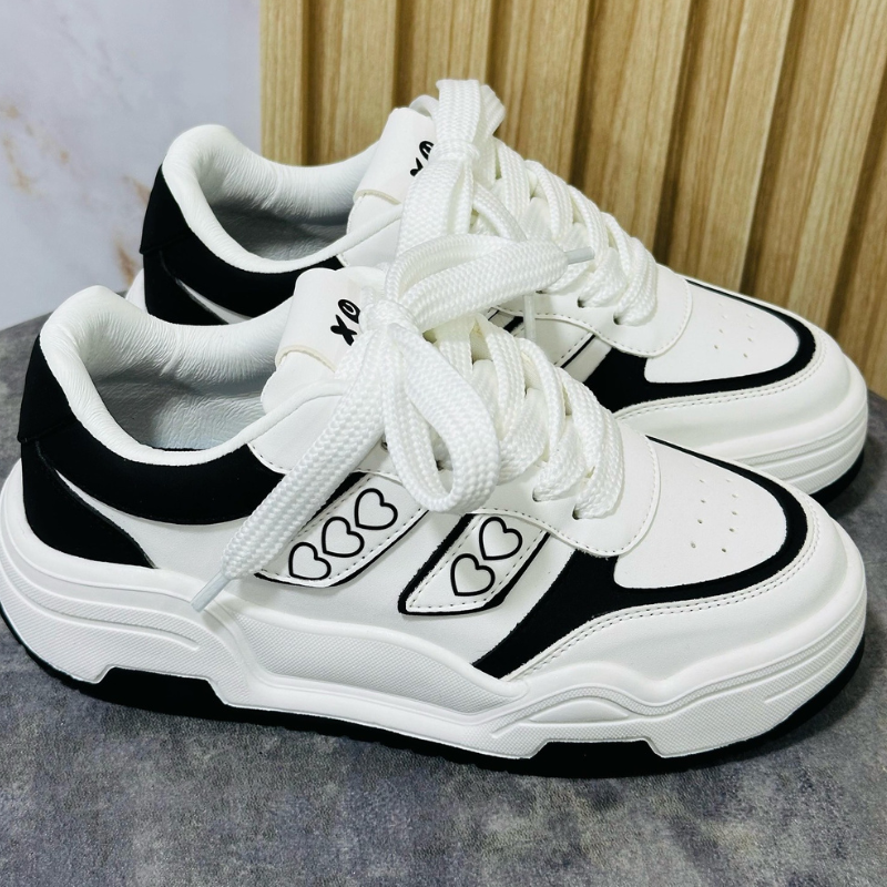 Tenis para mujer en color blanco con detalles negros y diseño moderno. Incluyen corazones negros en el lateral y son suela alta. Estilo urbano, cómodo y versátil de uso diario